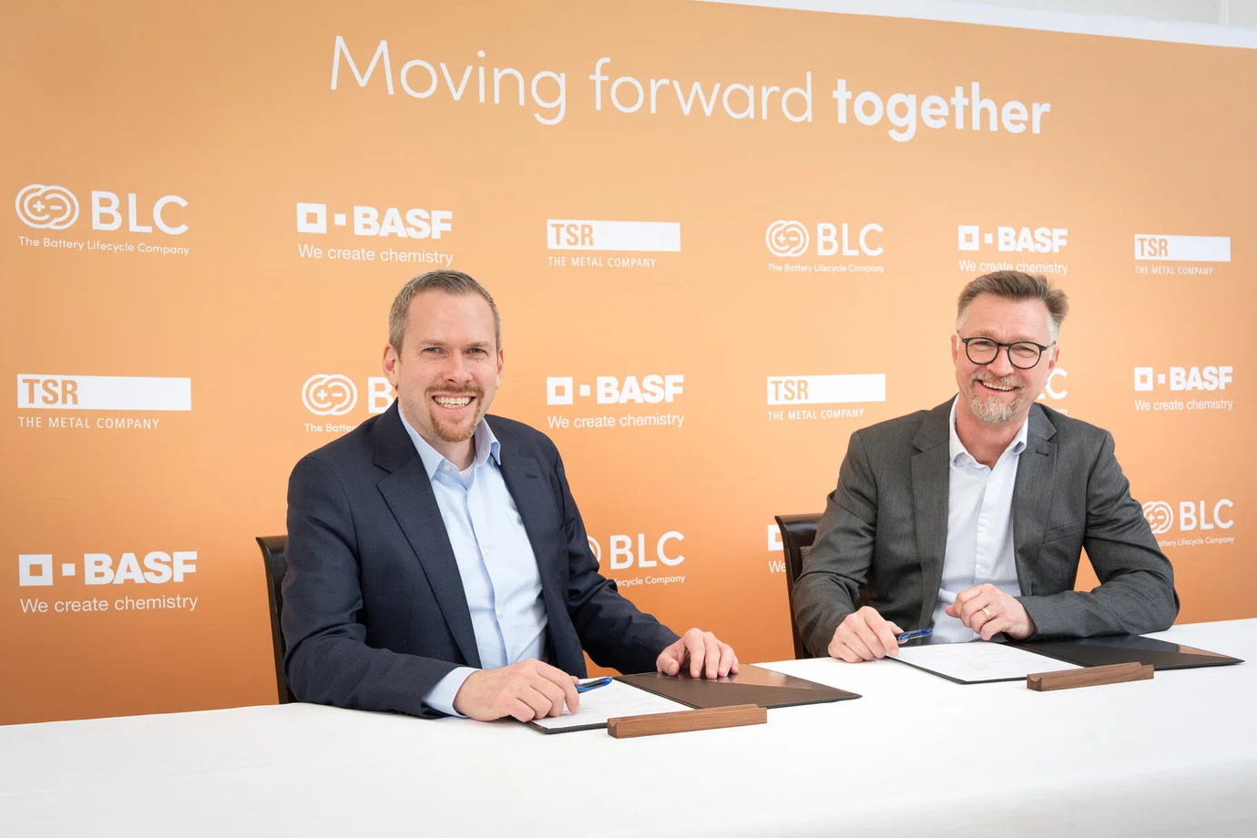 Geschäftsführer sitzen vor einer Wand mit der Überschrift "Moving forward together"