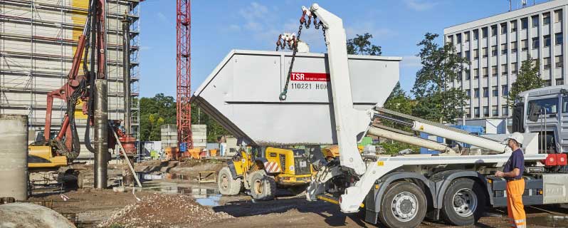 Beladener TSR Container wird von einem Kraftfahrzeug auf einer Baustelle abgeholt